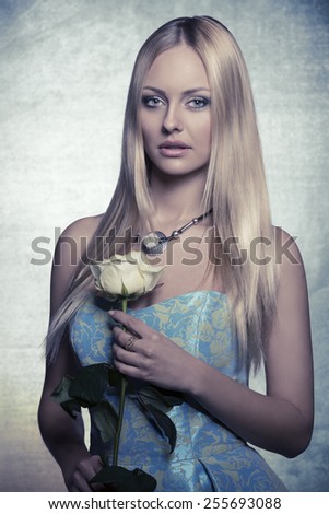 lovely blonde woman with long smooth hair and spring dress taking white rose in the hand and looking in camera. Romantic, fresh portrait