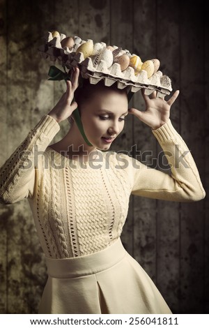 stylish brunette woman with yellow dress posing in easter shoot with easter eggs in the carton box on her head like a bizarre hat