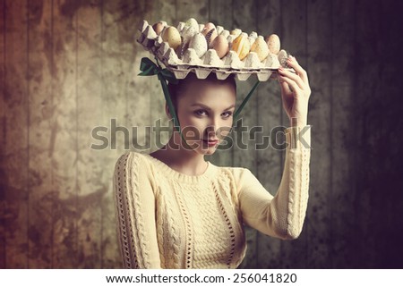 cute brunette female taking easter eggs box on the head like a bizarre hat, wearing yellow clothes and looking in camera. Funny portrait