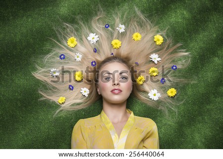 pretty blonde girl lying on green meadow posing with some colourful flowers in her long blonde hair