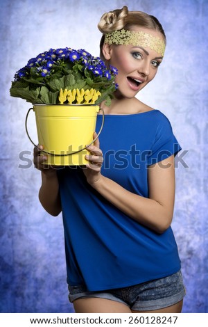 Pretty, fresh, spring blonde woman with nice hairstyle in blue t-shirt and yellow bucket of blue flowers with little rabbit decoration.