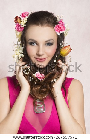 Pretty, natural, cheerful model with brown, curly hair with spring flowers. She wears pink dress with transparent part and nice silver necklace.