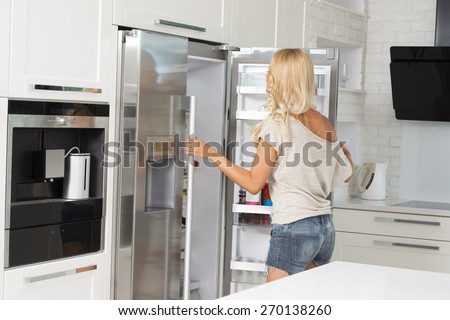 very pretty young blond woman , in act of opening her refrigerator , in moder luxory kitchen