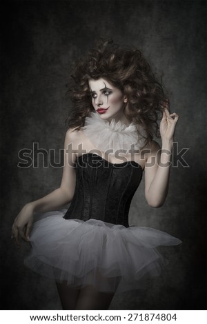 beautiful brunette girl with sad clown dancer masquerade, posing with vintage tutu, clown make-up and uncombed hair. Retro atmosphere