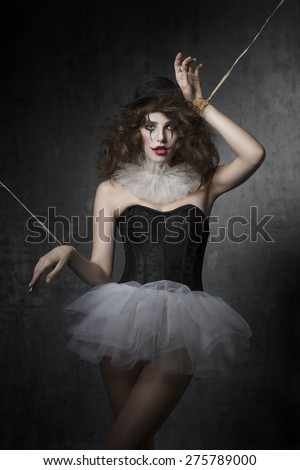 bizarre fashion portrait of brunette girl with gothic puppet costume. Wearing tutu, bowler hat and clown make-up. Uncombed hair, dark atmosphere