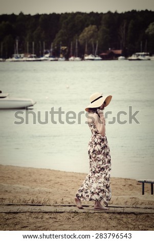 vintage images of a woman in summer dress walking on a lake beach with a natural hat near the water