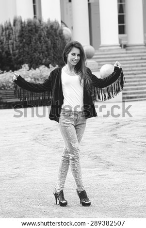 black and white fashion brunette woman with casual modern clothes and vintage jacket posing outdoor with old building on background. Long natural hair, stylish make-up