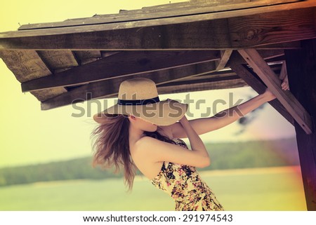 sensual young girl . near lake , wearing a summer hat and floral dress , she is covering her face . hair motion blur and forced color effect