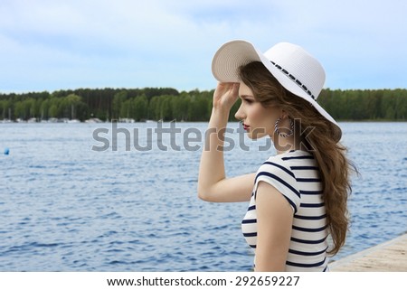 dreaming elegant woman , near the lake with line dress and white hat , she is looking away with thinking expression