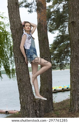 cute girl with urban summer style posing near tree in the nature with lake on background