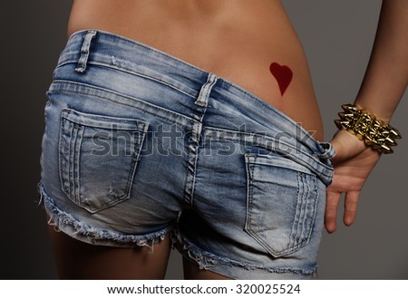 sexy woman with perfect ass showing her heart shaped tattoo on buttocks. Close-up of sexy bottom with denim shorts