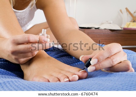 blond woman painting her feet nails on her bed