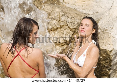 two sensual girls in bikini refreshing their body inside a waterfall