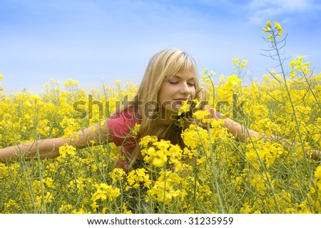 happy blond girl with open arms smelling some flowers in a yellow field