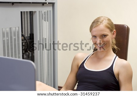 nice girl sitting at the leg press machine in a fitness club smiling in camera