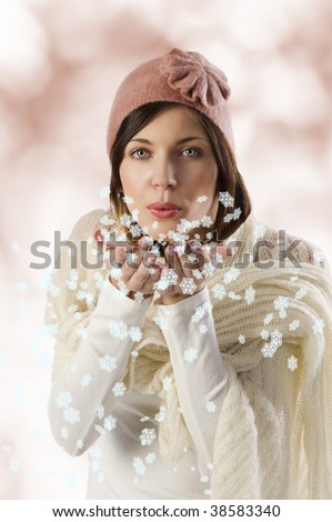 sweet pretty girl with white scarf and a pink winter cap blowing on snow flakes