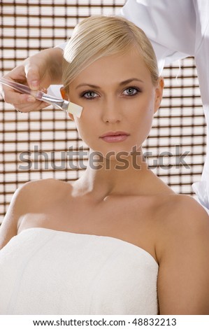 beauty advertising shot of a blond girl in act to be brushed from an assistant in a spa