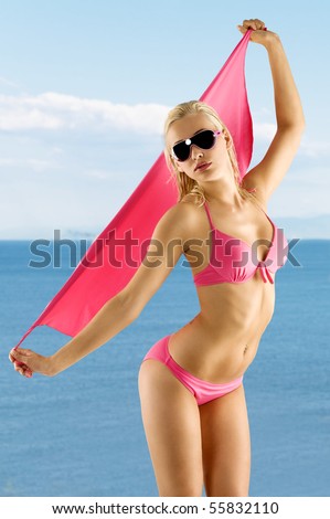 blond and attractive woman in pink bikini with sunglasses taking pose and playing with pareo