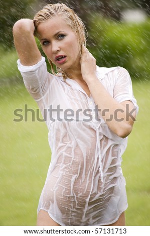 young sexy blond woman outdoor in a garden playing with water and rain with wet dress