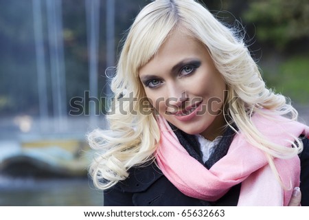 close up fashion portrait of a blond girl with hair style in black coat and pink scarf with forest in background