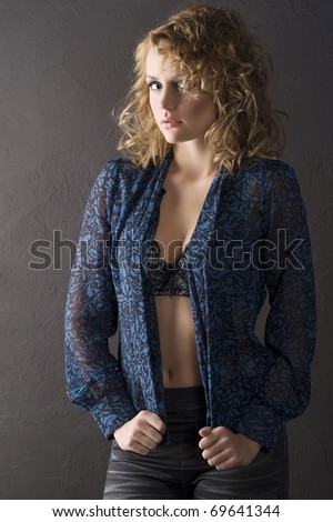 sexy blond curly haired woman in blue shirt and showing bra on black background