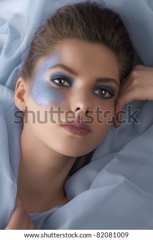 face shot of a pretty young woman with azure glitter make up and laying on fabric pieces