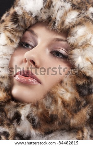 fashion close up portrait of a young pretty girl with a fur all around her face looking on one side