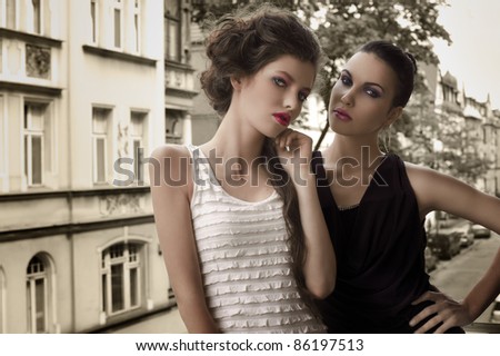 fashion shot of two attractive and elegant girl friend outside in a balcony with old fashion style building in background