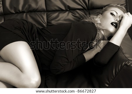 sensual blonde laying on a black leather couch wearing a black dress and black lipstick