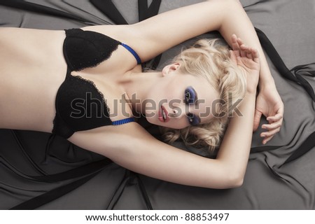 Sexy blond girl in black- blue bikini lingerie with hair style laying down on black material taking pose