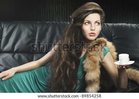 young elegant lady laying down on sofa keeping and drinking from a little cup of coffee. wearing green dress. she\'s lying on the sofa, looks at the left and takes a cup with left hand.