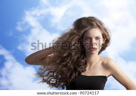 beauty fashion portrait of a very young cute brunette with long curly hair with hairstyle flying in the wind on sky background
