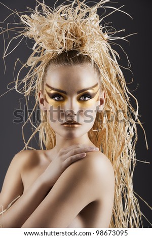 close  up of an amazing woman in ethnic style with creative make up and raffia on the head doing hairstylish. She is in front of the camera, looks in to the lens and has the right hand on the left