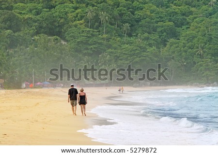 A couple take a walk along a tropical beach in Thailand. Rainforest in the background