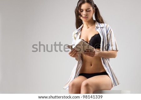 Tall sexy brunette woman in black lingerie and open shirt posing in a studio with a book