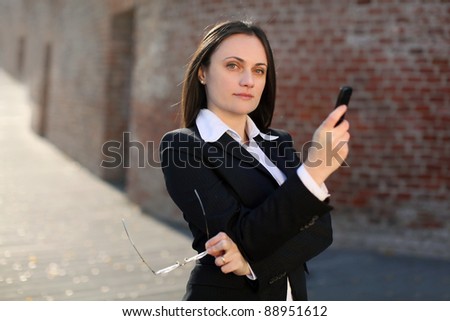 Businesswoman holding phone and glasses in front of a brick wall.