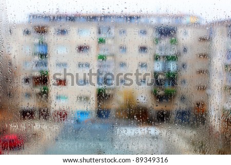 Rain drops are seen on a window with apartment flats in the background