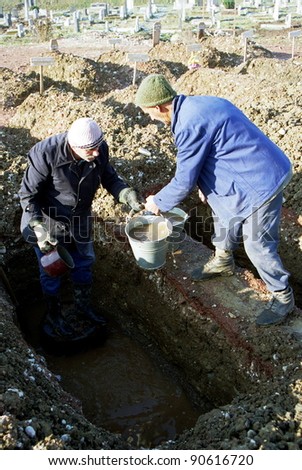 SARAJEVO, BOSNIA - DEC 12: Gravediggers bail water out of a frozen grave at cemetery on the grounds of the Olympic Stadium on Dec 12, 1992 in Sarajevo, Bosnia.