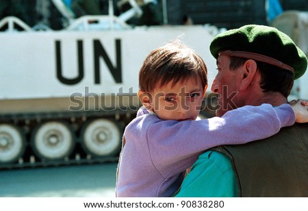 SARAJEVO, BOSNIA - JULY 19: A Bosnian boy and his father watch United Nations troop carriers drive through the besieged city on June 19, 1994 in Sarajevo, Bosnia.