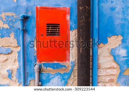 Colorful gas and water pipiline located on blue wall with red cabinet doors, Burano Venice
