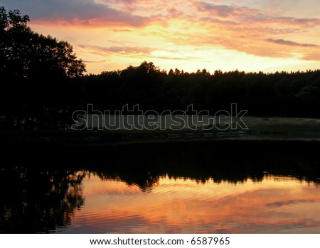 Sun is setting behind forest an is mirroring in the lake