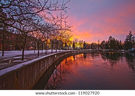 Bright yellow and pink sun setting over a river in a small city with reflection during winter.
