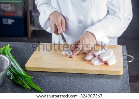 chef cutting raw chicken wing on chopping board