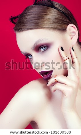the beautiful young girl with a tender face and a bright make-up, with cat's an ear, on a red background