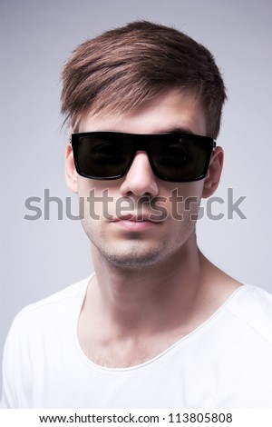 Close-up portrait of a young stylish beautiful  man with black glasses on a grey background