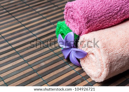 Spa towels rolls and flower lying on wooden mat. Space for your text. Horizontal composition.
