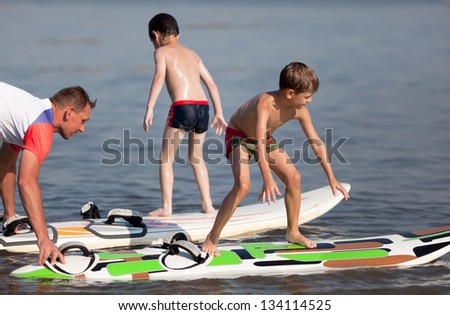 A two caucasian little boys are learning how to surf and are getting a lesson from a male instructor