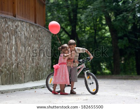Little boy with bike and little girl with balloon in their hands talking in the park