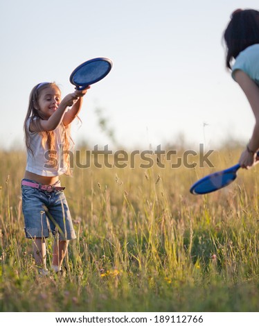 Mother and daughter playing tennis on the lawn in evening light