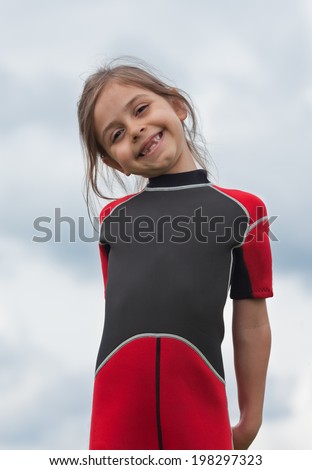 Cute little girl in wetsuit waiting for lesson windsurfing. Beautiful smile that is missing it\'s two front teeth